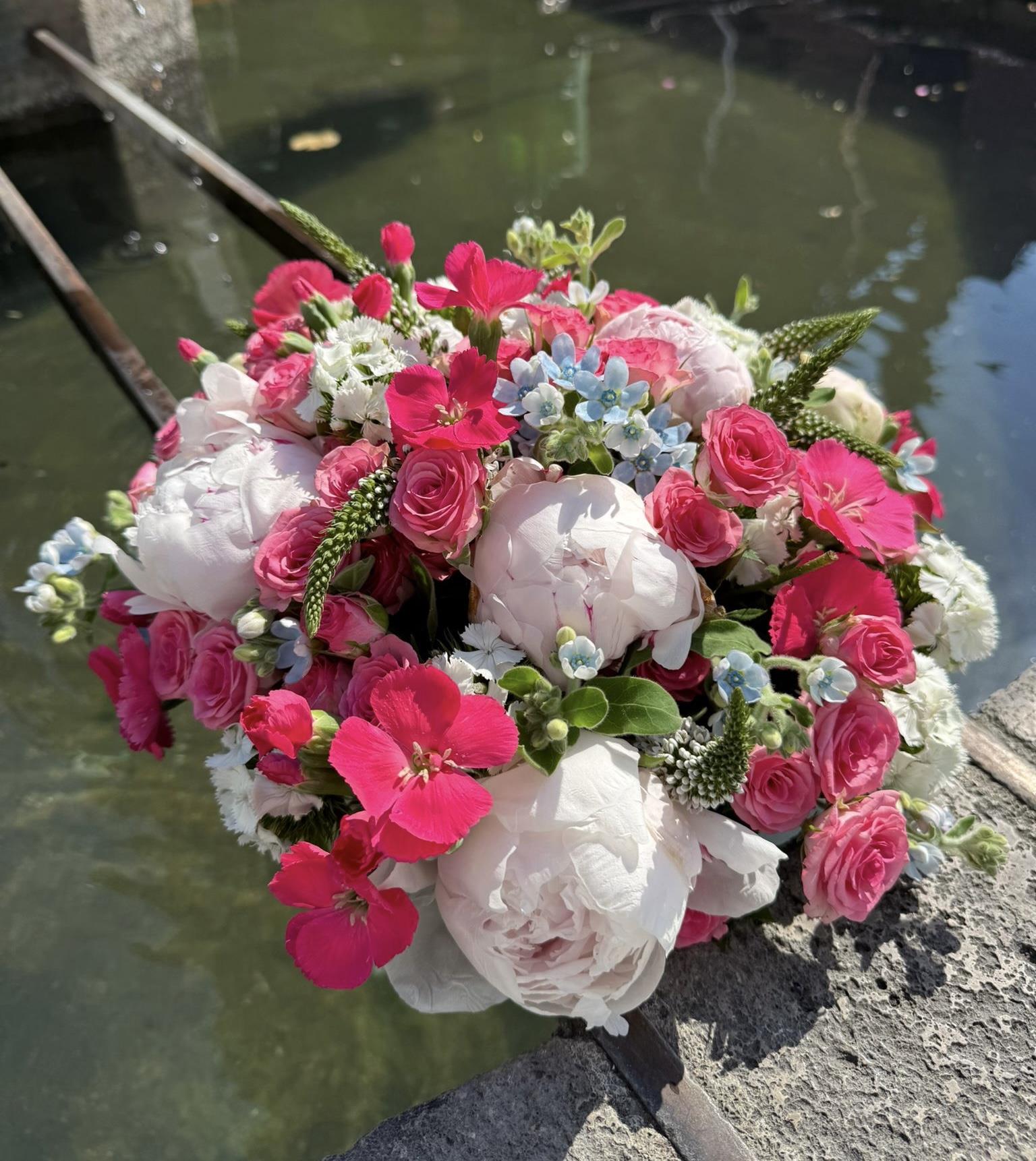 Runder Blumenstrauß mit rosa Rosen, weißen Pfingstrosen und feinem Grün am Brunnen auf dem Freiburger Münstermarkt