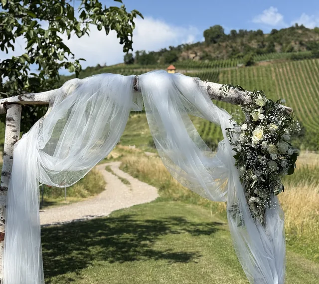 Hochzeitsbogen mit weißen Blüten und luftigem Stoff im Weinberg