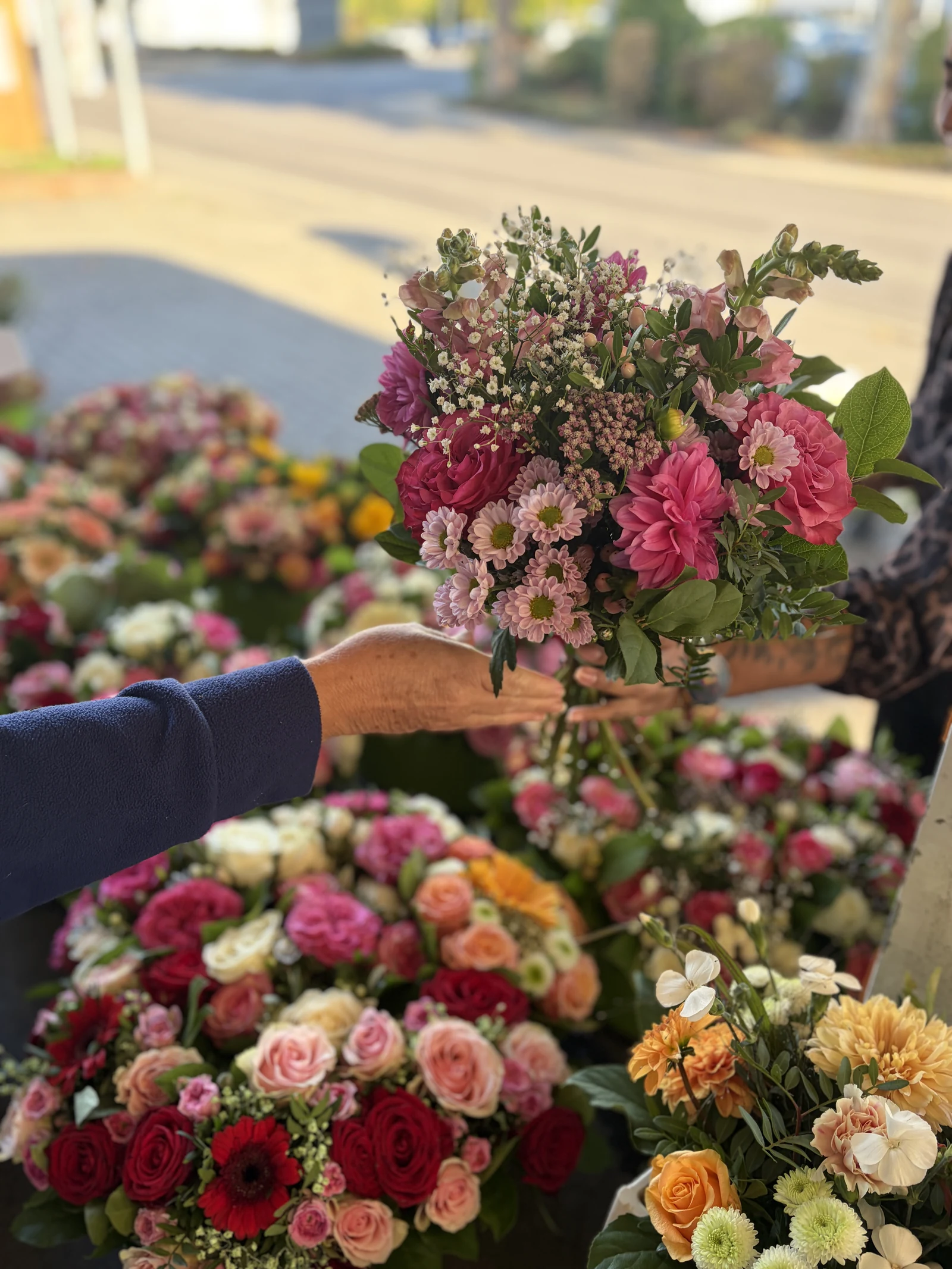Hände halten einen rosa Blumenstrauß über einer Auswahl bunter Sträuße am Marktstand